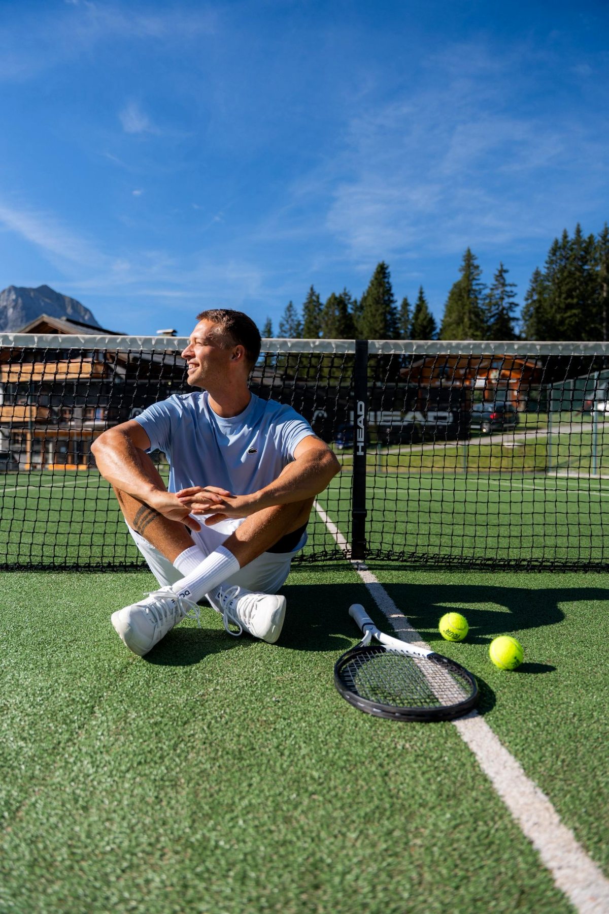 Julian Erhart sitzt am Netz auf dem Tennisplatz in Oberlech am Arlberg